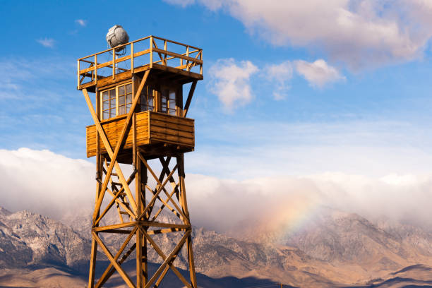A rainbow is forming in the Sierra Nevada Mountains behind a guard tower at Manzanar