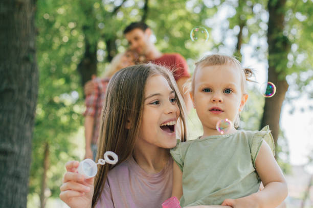 istock Happy girl making soap bubbles and looking at young sibling 969612504