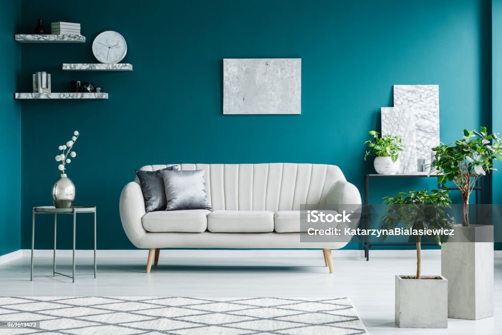Sofa between table and desk White sofa between a metal table and a black desk with paintings and plant in a turquoise living room interior Turquoise Colored Stock Photo