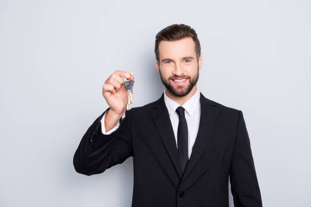 portrait of attractive stylish real estate with bristle, stubble in black tux, tuxedo and modern hairstyle having key from new house in hand isolated on grey background - house human hand choice real estate imagens e fotografias de stock