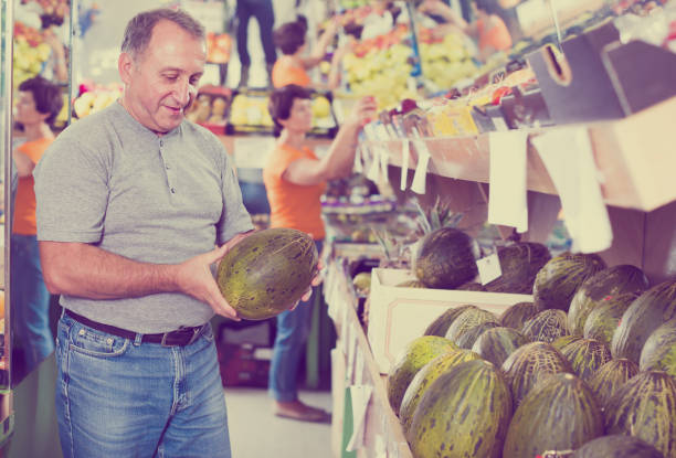 Glad man is choosing ripe melon in the store