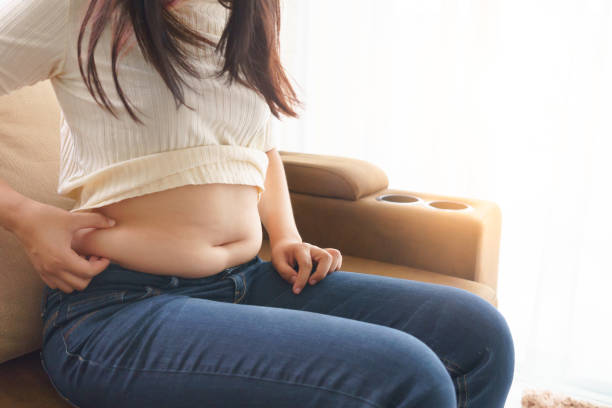 Woman holding her own belly when sitting down on sofa in the living room stock photo