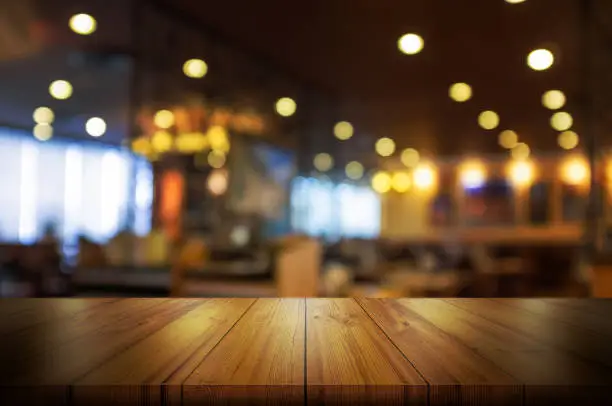 Photo of Empty wooden table top with blur coffee shop or restaurant interior background.