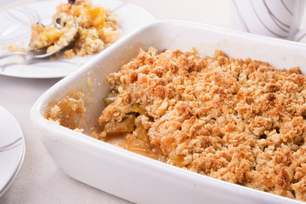 freshly baked apple crumble in a baking dish and a portion on a plate - crumble imagens e fotografias de stock