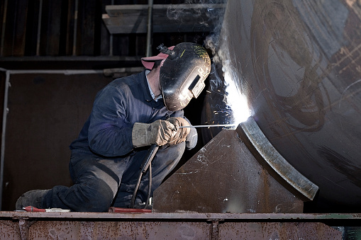 Trabajador con guantes y mascarilla de seguridad es soldar un pedazo grande de hierro en la industria del metal photo