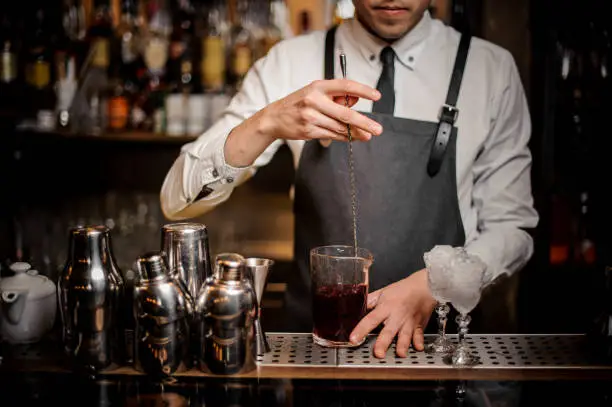 Photo of Bartender stirring a red alcoholic drink in the glass