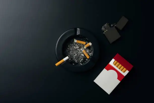 Photo of cigarette pack, chrome lighter and black ceramic ashtray full of ashes