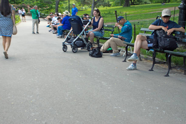 Outside outdoors in NYC New York City Central Park with many people and an asian man sitting on benches