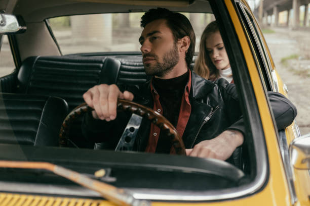 istock handsome young man driving retro car and girlfriend sitting behind 969696160