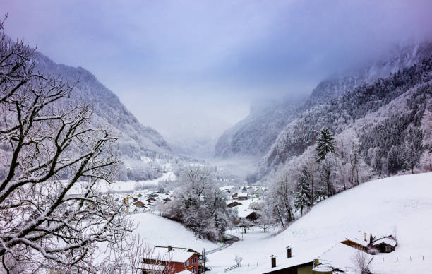 Morning fog blowing through a picturesque valley filled with snow covered chalets in Gsteigwiler, Switzerland.