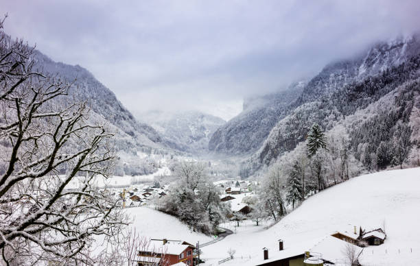 Morning fog blowing through a picturesque valley filled with snow covered chalets in Gsteigwiler, Switzerland.