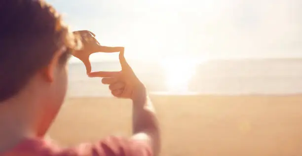 Photo of Future planning, hands making frame gesture with sunrise on sea summer