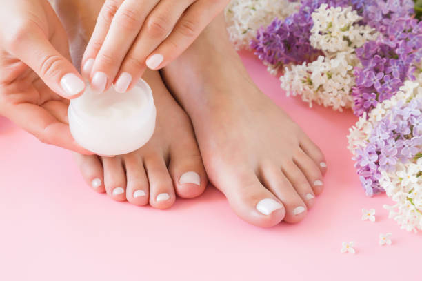 Young woman's hands applying perfect groomed feet with moisturizing natural cream. Care about clean, soft, smooth skin. Beautiful branches of colorful lilac. Fresh flowers on pastel pink background. Young woman's hands applying perfect groomed feet with moisturizing natural cream. Care about clean, soft, smooth skin. Beautiful branches of colorful lilac. Fresh flowers on pastel pink background. home pedicure stock pictures, royalty-free photos & images