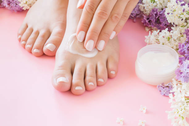Young woman's hands applying perfect groomed feet with moisturizing natural cream. Care about clean, soft, smooth skin. Beautiful branches of colorful lilac. Fresh flowers on pastel pink background. Young woman's hands applying perfect groomed feet with moisturizing natural cream. Care about clean, soft, smooth skin. Beautiful branches of colorful lilac. Fresh flowers on pastel pink background. ointment photos stock pictures, royalty-free photos & images