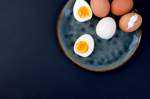 Boiled eggs on a plate and a black background. Fitness food, protein and yolk. Free space for text,