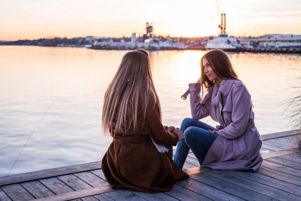 istock To friend sitting at pier and talking at sunset. 969844856