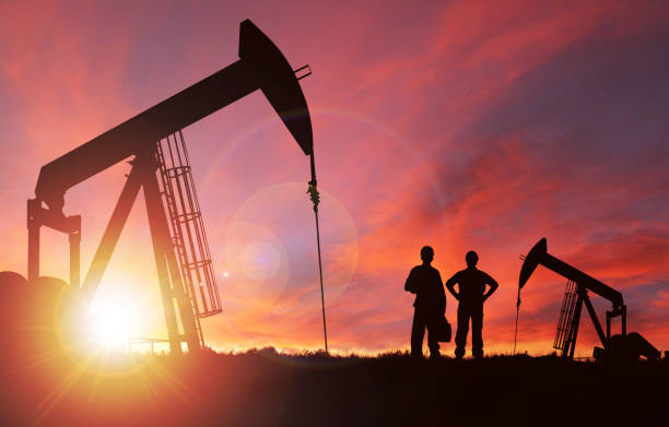 Sunset Over Pumpjack Silhouette With Copy Space Pump jack silhouette and hard hat workers against a sunset sky with deliberate lens flare and copy space. These jacks can extract between 5 to 40 liters of crude oil and water emulsion at each stroke. natural gas extraction stock pictures, royalty-free photos & images