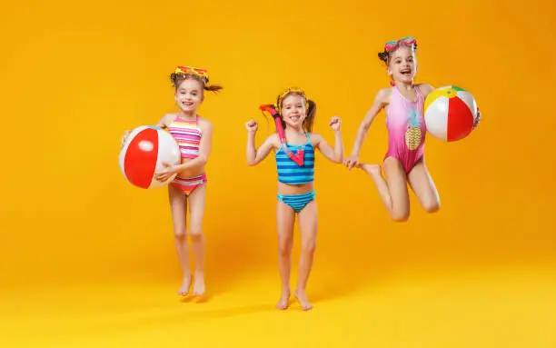 Photo of funny funny happy children in bathing suits  jumping  on colored background