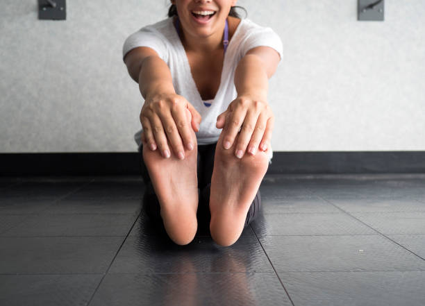 Smiling woman grabbing her feet to stretch hamstrings Smiling active woman grabbing her feet to stretch hamstrings in the studio touching toes stock pictures, royalty-free photos & images