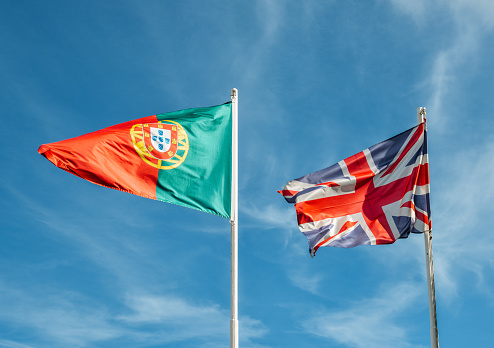 England and Portugal flag together on a mast against a blue sky.