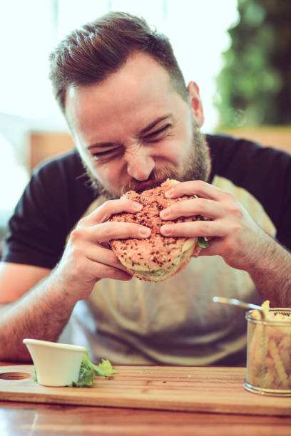 istock Handsome Male Eating A Cheeseburger In Fast Food Restaurant 969909384