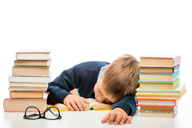 istock tired schoolchild is sleeping at a table between piles of books on a white background 969909628