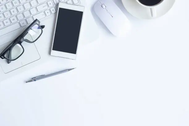 White desk office with laptop, smartphone and other supplies with cup of coffee. Top view with copy space for input the text. Designer workspace on desk top, view with essential elements on flat lay.