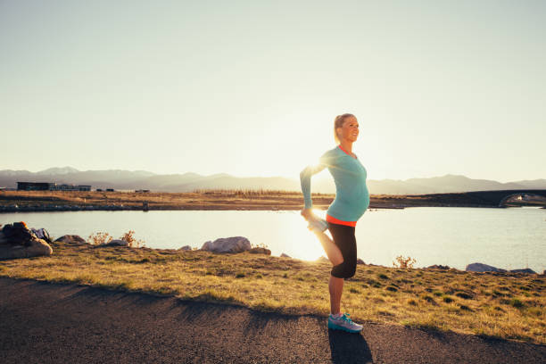 pregnant female runner stretches on a trail at sunset - nature human pregnancy color image photography imagens e fotografias de stock