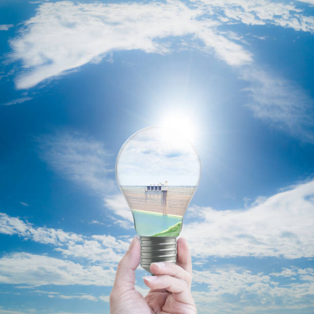 hand holding dam in light bulb on blue sky background. energy concept.
