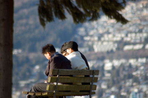 Friends, a senior and a young man sit in the park on a bench and talk in the autumn park.