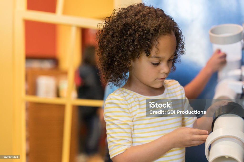 Adorable preschooler playing in discovery center Cute mixed race preschool plays with hands on exhibit at discovery center museum. she is concentrating while playing. Museum Stock Photo