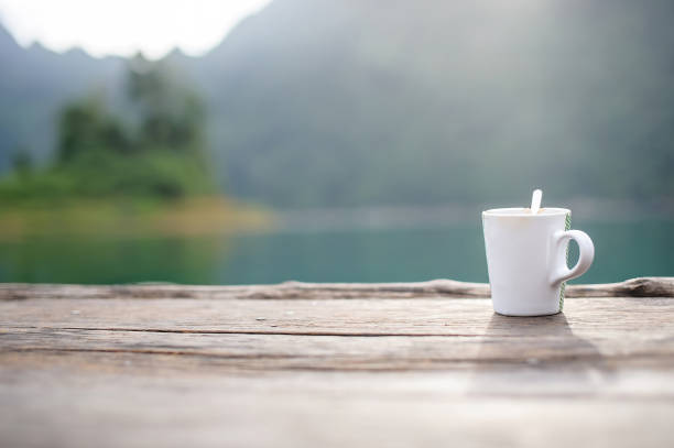 a cup of coffee in a blurry riverside view landscape background in sunshine with narrow depth of field - eyes narrowed imagens e fotografias de stock