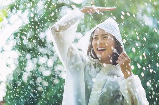 Rainy day asian woman wearing a raincoat outdoors. She is happy.