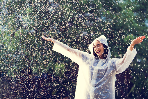 Rainy day asian woman wearing a raincoat outdoors. She is happy.