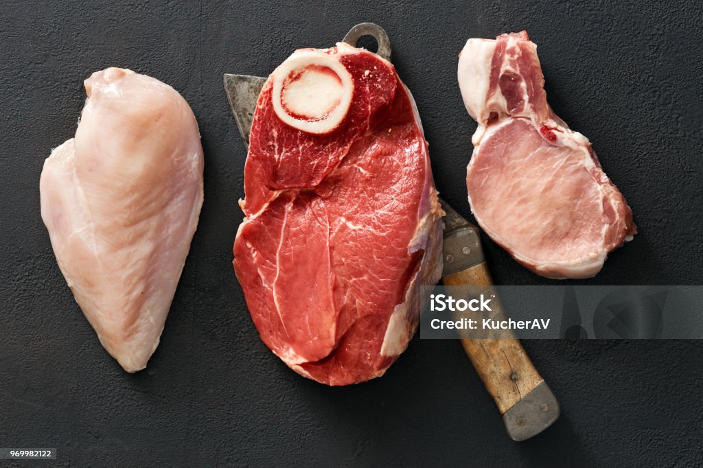 Variety of raw meat meat on bone, pork meat and chicken fillet Variety of raw meat beef meat on bone, pork meat and chicken fillet on dark stone background with butcher knife, top view Raw Food Stock Photo