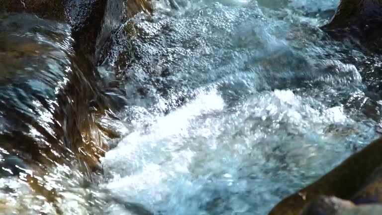 Rapid river water flowing between large stones creating white bubbling foam. Water stream flowing among stones in mountain river. Natural landscape