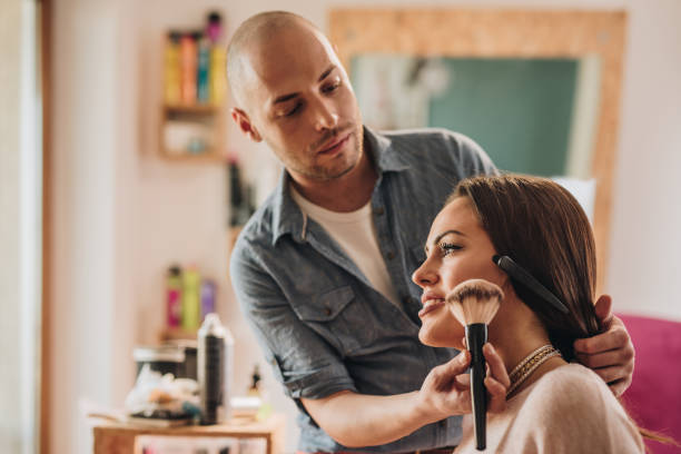 Male make-up artist applying blush on young woman's cheek. Beautiful woman enjoying in make-up treatment at beauty salon. makeup artist stock pictures, royalty-free photos & images