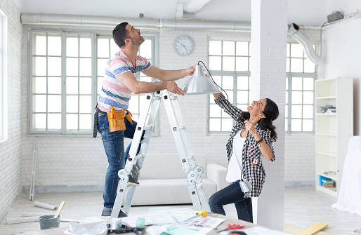 Couple hanging a lamp in new home, man on ladder.Property Services. New Home.