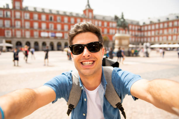 attractive young caucasian tourist student man having fun happy and excited taking a selfie with smart phone in plaza mayor, madrid, spain. travel,vacation, holidays in european city concept. - plaza mayor imagens e fotografias de stock