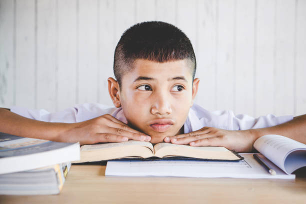 istock unhappy Asian boy student tired from reading book in a classroom 970049890