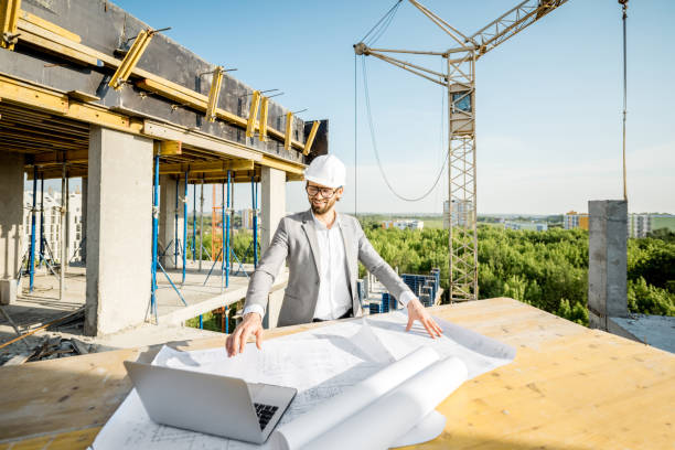 Engineer with drawings on the structure Handsome engineer working with architectural drawings at the table on the construction site outdoors general view stock pictures, royalty-free photos & images