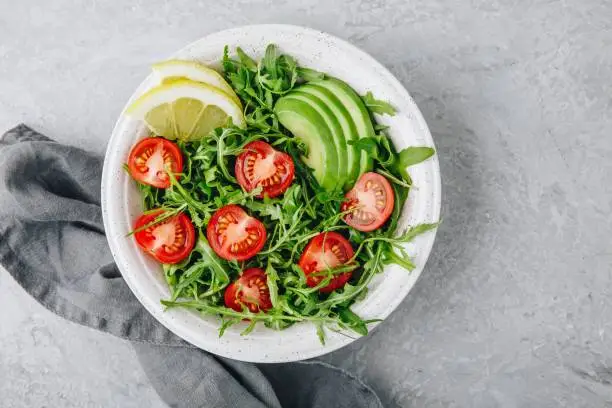 Green salad with leaves of arugula, tomatoes and avocado. Healthy summer lunch