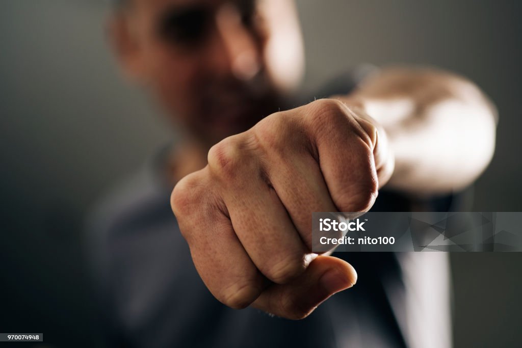 young man throwing a punch closeup of a young caucasian man throwing a punch to the observer, with a dramatic effect Fist Stock Photo