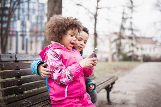 Cute, mixed race brother and sister, playing with mothers mobile phone outdoors in the park