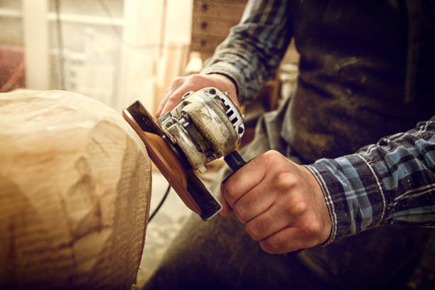 Close up of a carpenter, builder in work clothes saw to cut out sculpture from wooden a man's head  in the workshop, around a lot of tools,wooden,furniture for work