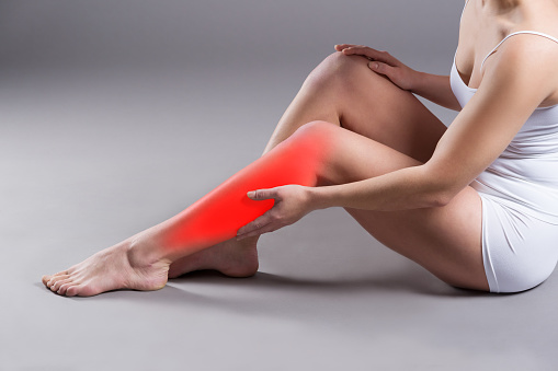 Pain in woman's shin, massage of female leg on gray background