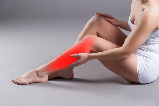 Pain in woman's shin, massage of female leg on gray background, studio shot with red dot