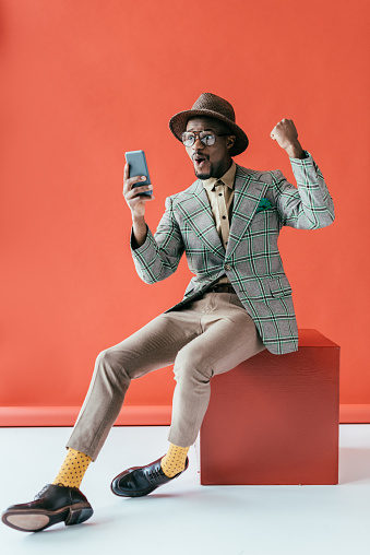 successful african american man in vintage jacket using smartphone, on red