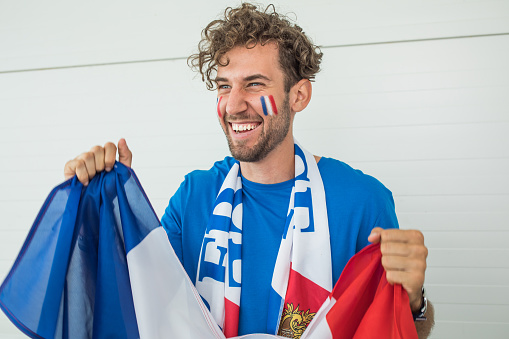 Soccer fan cheering at the game. Holding national team flag, with color paint on face. Studio shot