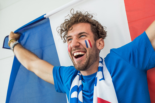 Soccer fan cheering at the game. Holding national team flag, with color paint on face. Studio shot